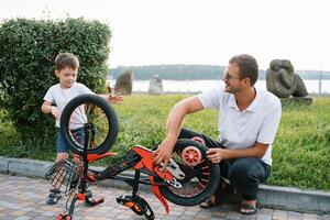 Happy father and his son having fun together at the green park, fixing bicycle together. father's day. photo