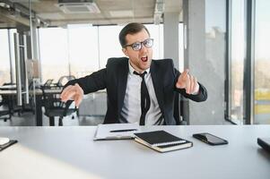 Angry senior businessman sitting at his desk and screaming photo