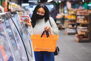 africano mujer vistiendo desechable médico máscara compras en supermercado durante coronavirus pandemia brote. epidemia hora foto