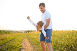 del padre día. contento familia padre y niñito hijo jugando y riendo en naturaleza a puesta de sol foto