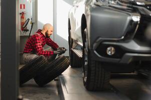 car mechanic screwing or unscrewing car wheel of lifted automobile by pneumatic wrench at repair service station photo