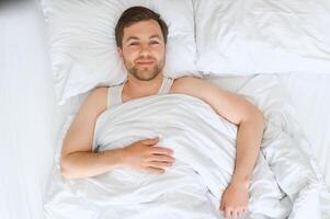 contento joven barbado hombre es relajante en el cama a hogar foto
