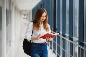 Positivity beautiful girl smiling at camera, standing on corridor with notes as backpack, going to lesson. Happy brunette female student studying in luxury university. photo