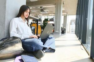 A beautiful caucasian female student is studying in college remotely. She is sitting with a laptop and a notepad and concentrated is watching a video conference lesson photo