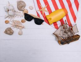 playa accesorios. toalla, chancletas, estrella de mar, barco y Gafas de sol en de madera antecedentes. parte superior ver con Copiar espacio. soleado tonificado foto