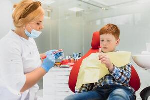 pediátrico dentista examinando un pequeño Niños dientes en el dentistas silla a el dental clínica foto