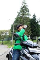 joven hombre moto conductor con en línea conductor aplicacion chaqueta bebida mineral agua foto