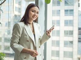 mujer de negocios hembra dama Mira a cámara contento sonrisa traje éxito hermosa bonito retrato oficina gerente estilo de vida tecnología teléfono inteligente móvil trabajo moderno ejecutivo atractivo pesebre empleo foto