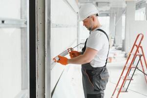 The builder fills the seam between plasterboard plates a silicone gun photo