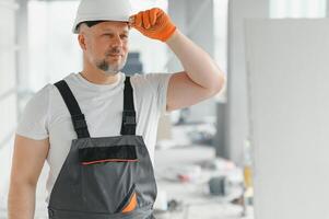 Portrait of a builder in working uniform with protective helmet standing with instruments at the construction site indoors photo