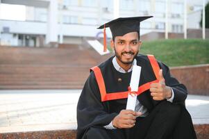 hermoso indio graduado en graduación resplandor con diploma. foto