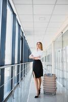 Portrait of successful business woman traveling with case at airport. Beautiful stylish female travel with luggage. photo