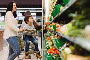 mujer y niño chico durante familia compras con carretilla a supermercado foto