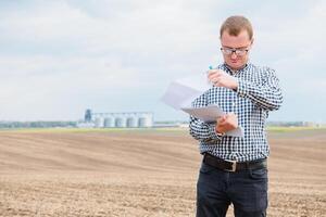 Happy farmer with laptop standing in wheat field in front of grain silo photo