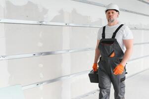 Portrait of a builder in working uniform with protective helmet standing with instruments at the construction site indoors photo