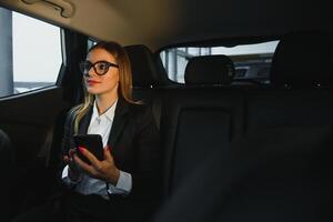 Some sort of interesting information. Smart businesswoman sits at backseat of the luxury car with black interior. photo