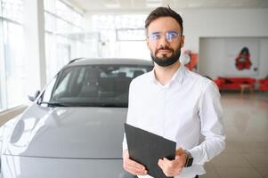 Smiling, friendly car seller standing in car salon. photo