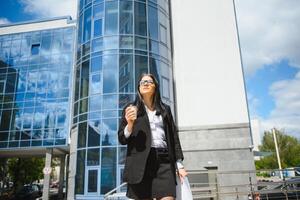 hermosa mujer yendo a trabajo con café caminando cerca oficina edificio. retrato de exitoso negocio mujer participación taza de caliente bebida en mano en su camino a trabajo en ciudad calle. alto resolución. foto