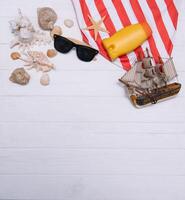 Beach accessories. Towel, flip-flops, starfish, boat and sunglasses on wooden background. Top view with copy space. Sunny toned photo