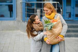 familia compras. madre y su hija son participación tienda de comestibles compras bolso con vegetales. foto