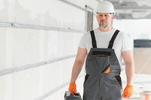 retrato de un constructor en trabajando uniforme con protector casco en pie con instrumentos a el construcción sitio adentro foto