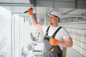 hombre ajuste arriba ventilación sistema adentro. un masculino trabajador instala aire ventilación tubería en un nuevo oficina edificio. foto