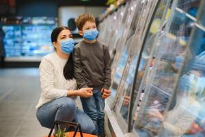 Shopping with kid during virus outbreak. Mother and child wearing surgical face mask buying fruit in supermarket. Mom and little boy buy fresh vegetable in grocery store. Family in shop photo