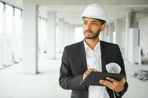 confidente asiático ingeniero hombre utilizando tableta para comprobación y mantenimiento a inspección a moderno hogar edificio construcción. arquitecto trabajando con blanco la seguridad casco en construcción sitio. foto