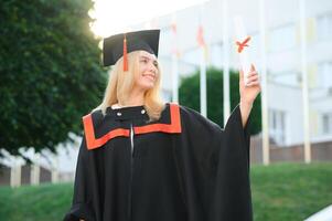 Portrait enthusiastic female college student graduate in cap and gown celebrating, holding diploma. photo