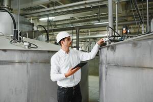 Close up of young Caucasian smiling worker with helmet on head using tablet for work while standing in warehouse. photo