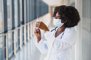 Young smiling African American doctor in medical mask holding a syringe photo