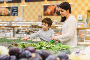 mujer y niño chico durante familia compras con carretilla a supermercado foto