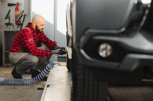 Mechanic changing a car tire in a workshop on a vehicle on a hoist using an electric drill to loosen the bolts in a concept of service or replacement photo