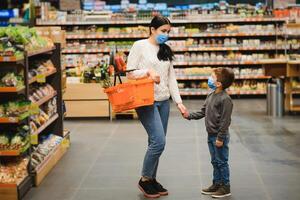 Mother and her son wearing protective face mask shop at a supermarket during the coronavirus epidemic. photo