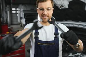 With tool in hand. Adult man in colored uniform works in the automobile salon photo