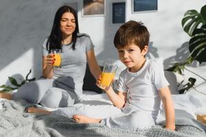 mom with son in pajamas drinking juice in the morning in bed. Healthy eating concept photo