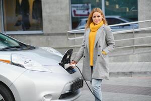 mujer cargando electro coche a el eléctrico gas estación. foto