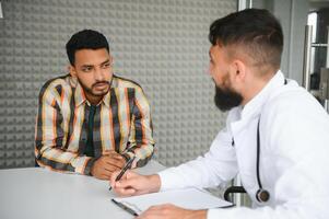 medicamento, cuidado de la salud y personas concepto - contento médico con portapapeles y joven masculino paciente reunión a hospital foto