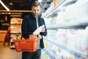 hermoso hombre comprando algunos sano comida y bebida en moderno supermercado o tienda de comestibles almacenar. estilo de vida y consumismo concepto. foto