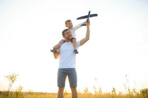 contento padre niño momento. padre llevar a cuestas su chico a puesta de sol mientras él es jugando con juguete avión. foto