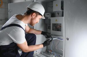 un masculino electricista trabajos en un tablero de conmutadores con un eléctrico conectando cable. foto