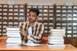 contento inteligente indio o árabe chico, mezclado carrera masculino, Universidad alumno, en el biblioteca foto