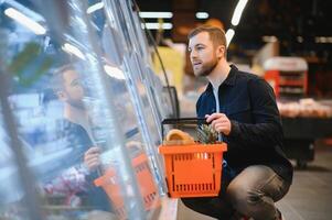 Young man buying groceries at the supermarket. Other customers in background. Consumerism concept. photo