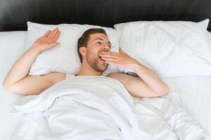 joven hombre dormido despertar arriba y extensión en su cama foto