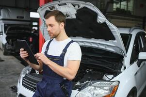 Automobile computer diagnosis. Car mechanic repairer looks for engine failure on diagnostics equipment in vehicle service workshop photo