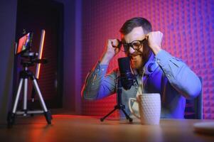 Young man recording or streaming podcast using microphone at his small broadcast studio. Content creator. photo