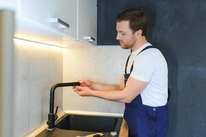 joven reparador instalando grifo de cocina lavabo en cocina habitación foto