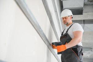 man drywall worker or plasterer putting mesh tape for plasterboard on a wall using a spatula and plaster. Wearing white hardhat, work gloves and safety glasses. Image with copy space. photo