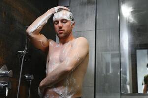 Handsome Young Man Taking A Shower Standing Under Falling Water Drops Washing Naked Body And Head In Modern Bathroom At Home. Male Model photo