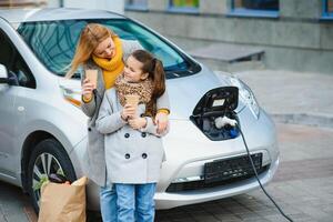 mother with daughter charging electro car at the electric gas station and speak on mobile phone photo